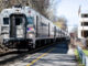 A commuter train wails its approach to Emerson Station downtown on April 13, 2024, arresting road traffic. The borough's mixed-use-redevelopment project, at right, on Kinderkamack between Lincoln and Linwood, languishes under construction with its principals tied up on cash flow and legal issues, some with the borough. John Snyder photo.