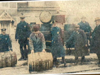 The raiding party with barrels seized at the V.M. road house on Old Hook Road on Jan. 17, 1925. Approximately 400 gallons of liquor were poured out on Center Avenue. Left to right: P.O. Butterfield, Marshal Allison, Police Commissioner Wyks, P.O. Bartz, Special Officer Frontera, Judge Ruckner, and Mayor Brickell. The building in the background is the Westwood Firehouse that stood on Center near Jefferson Avenue, about where the modern firehouse stands.