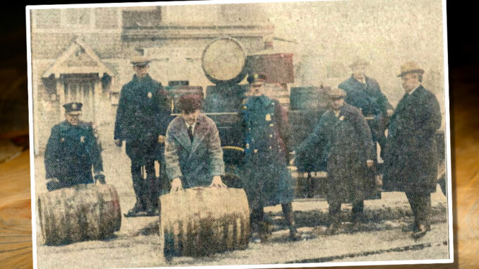 The raiding party with barrels seized at the V.M. road house on Old Hook Road on Jan. 17, 1925. Approximately 400 gallons of liquor were poured out on Center Avenue. Left to right: P.O. Butterfield, Marshal Allison, Police Commissioner Wyks, P.O. Bartz, Special Officer Frontera, Judge Ruckner, and Mayor Brickell. The building in the background is the Westwood Firehouse that stood on Center near Jefferson Avenue, about where the modern firehouse stands.