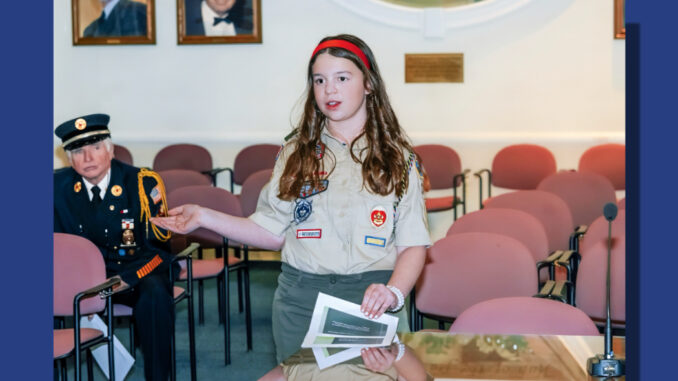 With 50-year Westwood firefighter JayMee Hodges looking on, Westwood Troop 321 Life Scout Bella Tirri, grade 8, presents on her work for the Westwood Heritage Society at the Dec. 16, 2025 meeting of the governing body. John Snyder photo.