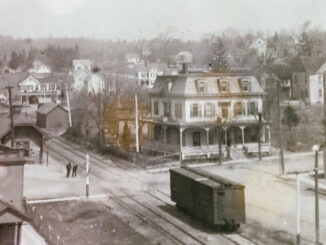 The Park Avenue railroad crossing in the 1910s. The road coming up from the bottom right corner is Broadway, then called Railroad Avenue, and it meets up with Park Avenue, which runs horizontally. At far left we see a portion of the Mittag & Volger typewriter ribbon factory. Behind where the men are standing is the Park Ridge train station. The three-story, Second Empire-style building across from Broadway was a hotel.