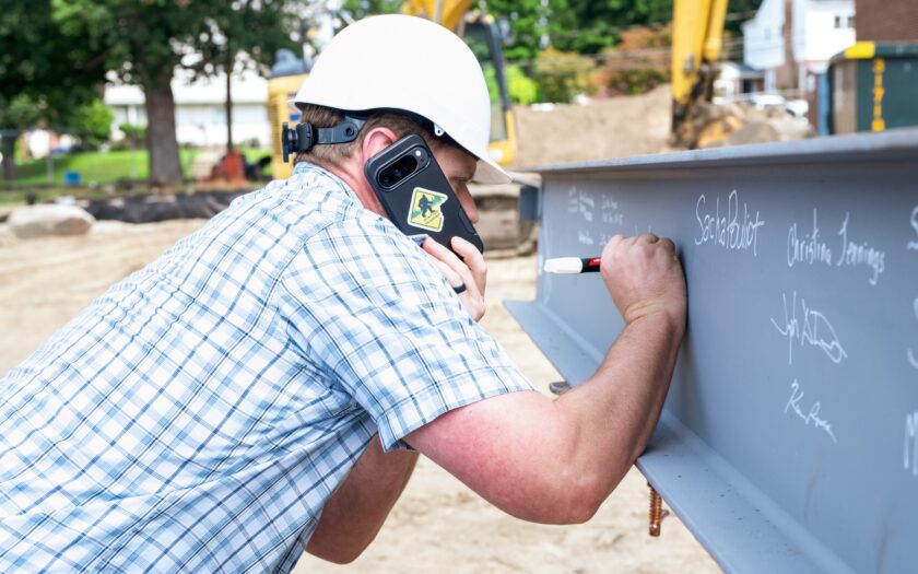 Even as the ceremonial beam signing unfolded around him, a construction worker stayed on the job — cellphone to his ear as he added his own name to the steel. The moment captured both the significance of the milestone and the work still underway at George G. White Middle School. John Snyder photo.