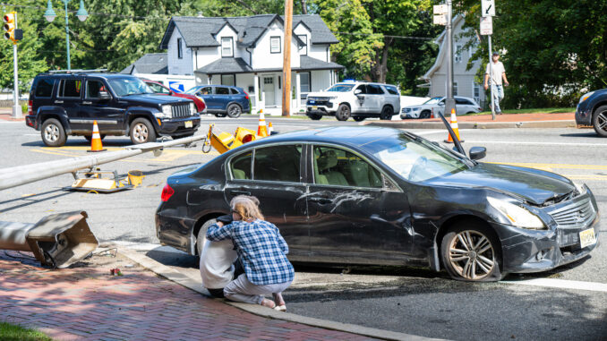 A driver is consoled beside his damaged Infiniti after striking a traffic light stanchion at Kinderkamack Road and New Milford Avenue in Oradell on Sept. 24. The crash brought down the signals, a camera and a delayed-green warning sign. Police Chief David Gangemi said the driver was uninjured. Photo by John Snyder.
