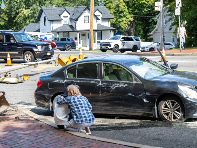 A driver is consoled beside his damaged Infiniti after striking a traffic light stanchion at Kinderkamack Road and New Milford Avenue in Oradell on Sept. 24. The crash brought down the signals, a camera and a delayed-green warning sign. Police Chief David Gangemi said the driver was uninjured. Photo by John Snyder.