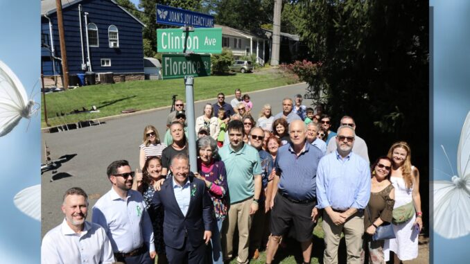 Rosemarie D’Alessandro, center in a butterfly-patterned dress, gathers with officials, friends and supporters beneath the newly unveiled “Joan’s Joy Legacy Lane” sign Sept. 7. The dedication, held on her daughter Joan’s birthday, honors the foundation Rosemarie built in her memory and its work for child safety. Anthony DeRosa photo.